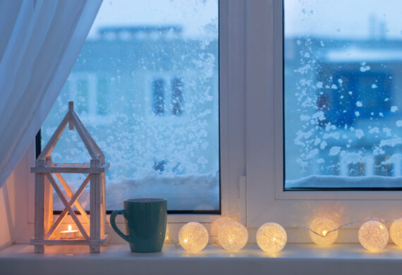 Inside shot of windows which are covered with snow on the outside and a warm cup of coffee inside