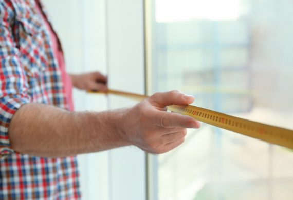 Man with a tape measure measuring the size of a window