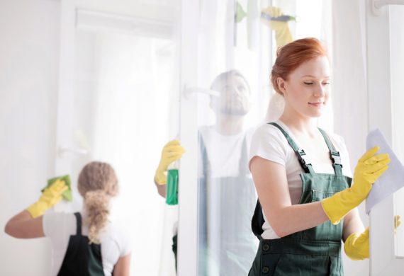 Red headed woman cleaning UPVC window frames while a man cleans the window in the background