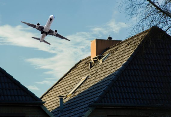 A plane flying closely over a roof on a home